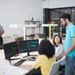 Office employees collaborate on financial data at modern workspace, engaging in teamwork and communication.